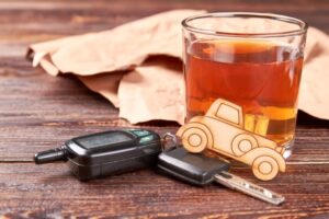 Alcohol glass, car model, and car keys on a table representing impaired driving laws explained by a San Diego criminal defense attorney.