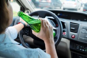 Person holding an alcoholic drink while behind the wheel, illustrating DUI laws explained by a San Diego criminal defense attorney.
