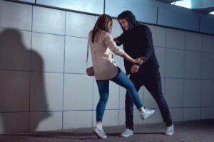 Woman kicking an individual in a hoodie to illustrate self-defense versus assault, explained by a San Diego criminal defense attorney.
