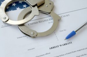 Criminal case document with handcuffs placed on top, illustrating bench warrant vs. arrest warrant, explained by a Carlsbad criminal defense attorney.